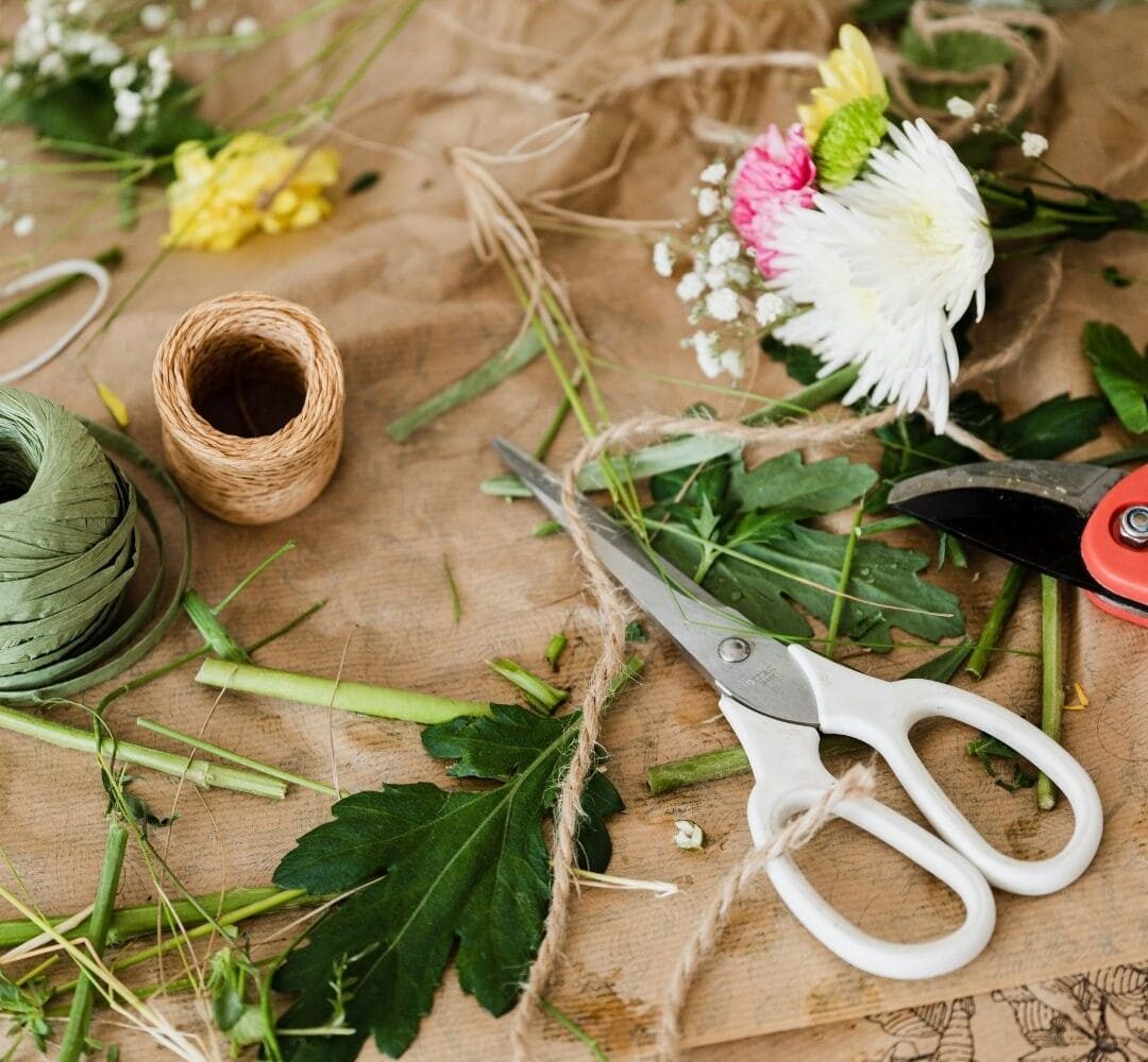 Matériel de fleuriste avec tiges coupées, ficelles, feuilles et ciseaux sur une table en bois